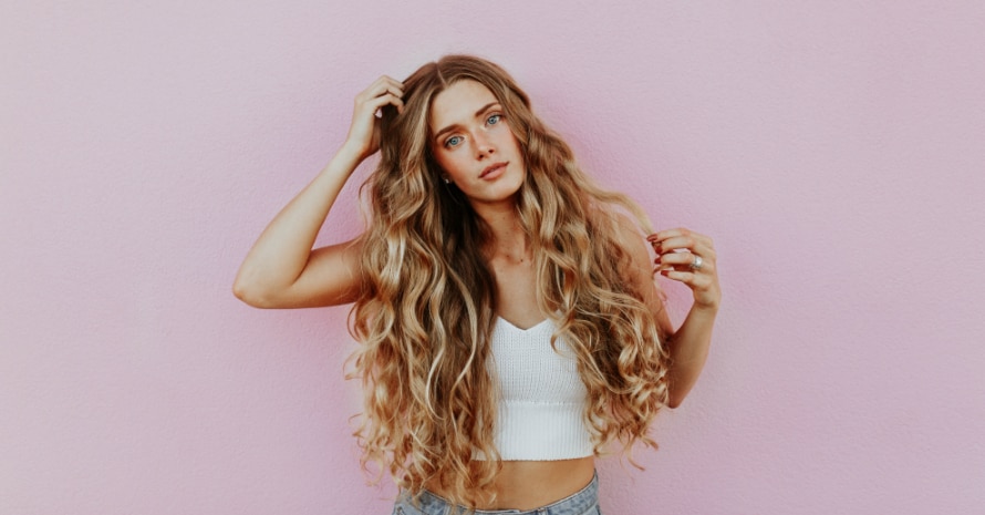 Woman standing next to pink wall while scratching her head